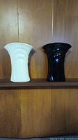 Pair of black and white ceramic vases placed on a wooden shelf, showing their shape and size.