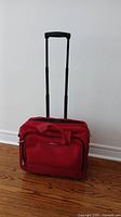 Red roller suitcase standing upright with extended retractable handle, showing front compartments and textured fabric.