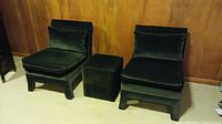 Front view of two deep blue/black velvet slipper chairs with matching ottoman cube in between on tan carpet.