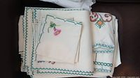 Stack of needlepoint napkins and placemats with green cross-stitch border and floral corner motifs
