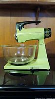Side view of vintage avocado green Mixmaster stand mixer with glass bowl attached, showing overall design.