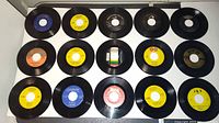 Top-down view of 20 vintage 45rpm vinyl records arranged in four rows of five, showing labels from various record companies including Decca, RCA, and others.