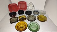 Front view of the 14 vintage cigarette ashtrays showing variety of color, shapes, and logos.