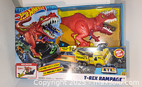 Front view of boxed Hot Wheels T-Rex Rampage toy set showing red dinosaur and yellow vehicle