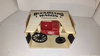 Photo of the Buckboard Wagon toy in original box showing red body, black wheels, and Agway logo.