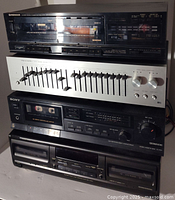 Stack of four vintage audio components: Pioneer stereo tuner on top, Realistic graphic equalizer below it, then Sony cassette deck, and another black cassette tape player at the bottom. All components show typical signs of age and usage.
