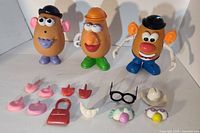 Three Mr Potato Head figures displayed with multiple facial features and accessories laid out in front including ears, noses, lips, glasses, and hats.