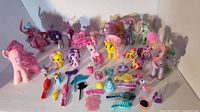Image showing the collection of approximately 20 My Little Pony figures and numerous small accessories including hairbrushes, combs, and miniature toy items.
