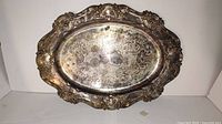 Silver plated bronze dinner plate, oval shape, with ornate detailed rim and engraved decorative center. Tarnished surface, needs cleaning.