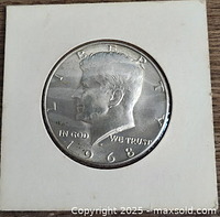 Obverse side of the 1968-D Kennedy half dollar coin in a white cardboard holder showing the profile of John F. Kennedy and inscriptions.