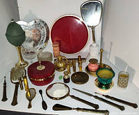 Full view of all items in the vintage women's vanity beauty lot arranged on a white surface. Includes mirrors, brushes, lamp, and various cosmetic containers.