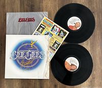 Two black vinyl records with BeeGees labels, original album cover showing BeeGees Greatest artwork, white inner sleeve with BeeGees text, and promotional insert sheet with colorful graphics.