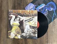 Front cover of Bob Dylan album Knocked Out Loaded with vinyl partially removed showing red label and an inner sleeve that features a photo of Bob Dylan singing on stage.