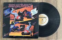 Vinyl LP record and original Breakdance album sleeve together on wood surface.