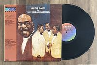 Vinyl LP record with cover featuring Count Basie and The Mills Brothers artwork, partially pulled out to show the record label.