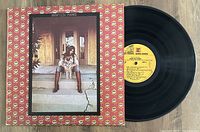 Vinyl record partially removed from the original album jacket showing cover art and yellow label on the record