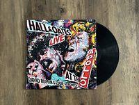 Photo of the front cover and vinyl record of Hall & Oates 'Live At The Apollo' album showing colorful illustrated artwork and black vinyl disc.