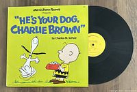 Vinyl LP record titled 'He's Your Dog Charlie Brown' with colorful yellow cover showing Snoopy and Charlie Brown, along with the black vinyl disc partially visible.