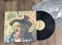 Vinyl LP record with cover showing John Denver, record partially pulled out showing label with track information.