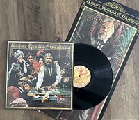 Photo of the vinyl LP album and poster for Kenny Rogers' "The Gambler" showing the record partially out of its sleeve with album cover visible and folded poster underneath.