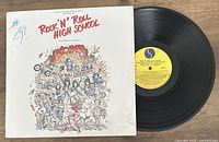 Vinyl LP and cover for Rock 'N' Roll High School original soundtrack. Cover has cartoon-style artwork and writing in blue pen. Record label is yellow with text.