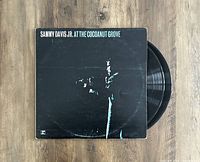 Top-down photo of the album cover with part of two vinyl records showing on the right side, on a wooden surface.