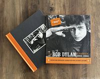 Photo of the closed hardcover Bob Dylan Scrapbook showing the cover image and the orange spine with title.