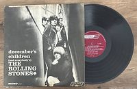 Black and white album cover of December's Children by The Rolling Stones with the vinyl LP partially visible beside it on a wooden surface.