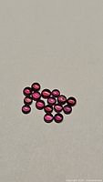 Fifteen small round cabochon red pink sapphires arranged on a flat surface.