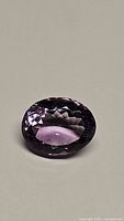 Close-up photo of a deep purple natural amethyst gemstone cut in an oval shape, showing clean facets and good clarity.