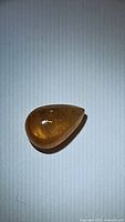 Photo of pear-shaped cabochon yellow-orange sapphire showing inclusions and color under light on plain background.