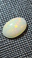 Close-up photo of natural oval cabochon Ethiopian opal showcasing multicolored flashes on textured black background.