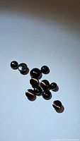 Overview of 11 small round cabochon jet black onyx gemstones scattered on white background.