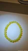 Top-down photo of natural lemon jade bracelet with uniformly sized round yellow beads on white background