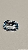 Oval cut natural blue topaz gemstone on a plain background, showing its color and clarity.