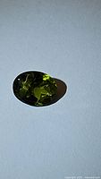 Close-up of the natural peridot gemstone showing its oval cut and apple green color on white background with shadows.