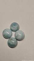 Four round, polished natural Larimar cabochon gemstones placed together, showing their size and typical blue and white marbled coloration.