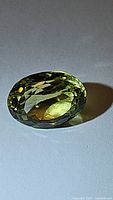 Close-up image of the faceted oval lemon citrine gemstone displaying its light yellow-green color and facets.