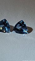 Clear image showing the matching pair of trillion cut Swiss blue topaz gemstones on a neutral background with light reflections highlighting facets.