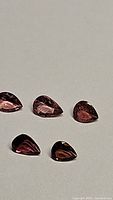 Photo showing five natural pink tourmaline gemstones, pear-shaped and faceted with varying pink shades.