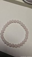 Natural rose quartz stretchy bracelet laid out in a circular shape on a white surface, showing smooth, round pink beads approximately 6mm in size.