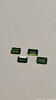 Four natural emerald cut chrome diopside gemstones laid out on a white background, showing their bright green color and rectangular shape.
