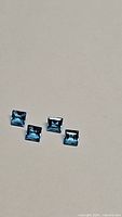 Four square cut natural Swiss blue topaz gemstones arranged on a plain background, showing facets and color under bright light.
