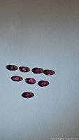 Seven marquis cut natural untreated rubies displayed on a white surface showing their red-pink color and size.