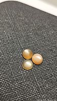 Three round cabochon peach moonstones with light flash, arranged close together on textured dark fabric background.