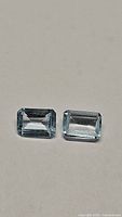 Two natural sky blue topaz gemstones shown side by side on a neutral background highlighting their emerald cut and sky blue color.