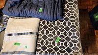 Photo shows all three blankets: a dark blue Casper weighted blanket, a woven beige and black blanket with a stain, and a gray and white plush blanket with geometric pattern.