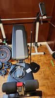 Wide view of Bowflex workout bench with AI Case phone/tablet stand beside it, metal hooks/rings on bench seat, and weight plates nearby.