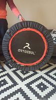 Front view of folded mini trampoline with black jumping mat and Artesol logo, complete round frame with orange accent and black padding.