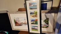 Photo showing three prints: a large horizontal Toronto skyline, and a vertical triptych of Vancouver scenes.